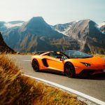 an orange sports car driving down a mountain road
