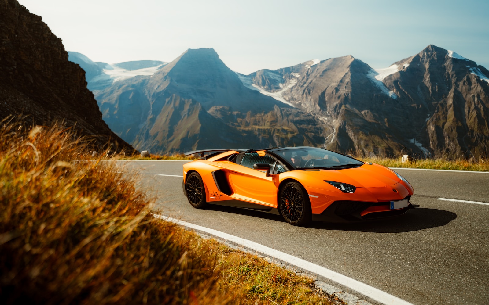 an orange sports car driving down a mountain road