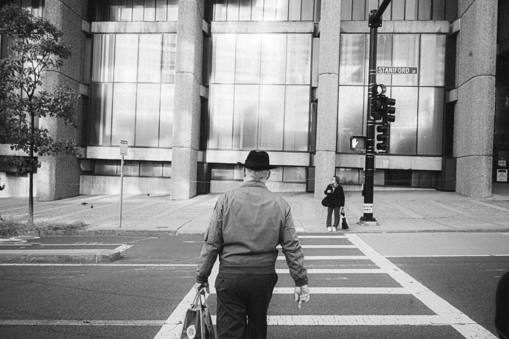 a man walking across a cross walk in front of a tall building