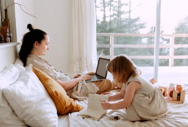 Mother working remotely while daughter drawing nearby