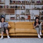 A Mother and Daughter Sitting on the Couch while Using a Laptop and Reading a Book