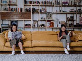 A Mother and Daughter Sitting on the Couch while Using a Laptop and Reading a Book