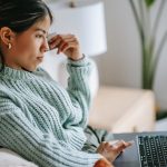 Side view of crop concentrated young ethnic female using touchpad of netbook and shopping online