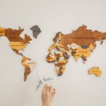 Crop unrecognizable person with toy aircraft near multicolored decorative world map with continents attached on white background in light studio