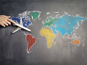Top view of crop anonymous person holding toy airplane on colorful world map drawn on chalkboard