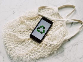 Overhead of smartphone with simple recycling sign on screen placed on white eco friendly mesh bag on marble table in room