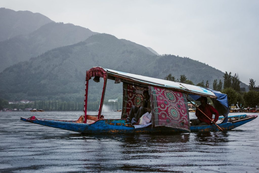 Anonymous ethnic men in roofed boat on lake against ridge