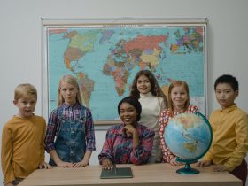 Teacher and a Group of Children Standing Beside Table With Globe