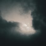 a dark sky with clouds and a half moon