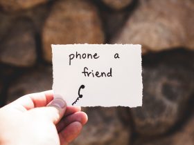 person holding piece of paper with phone a friend written text