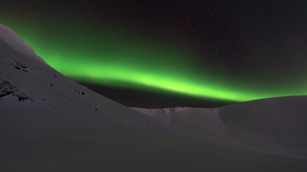 a green aurora bore in the sky above a snow covered mountain